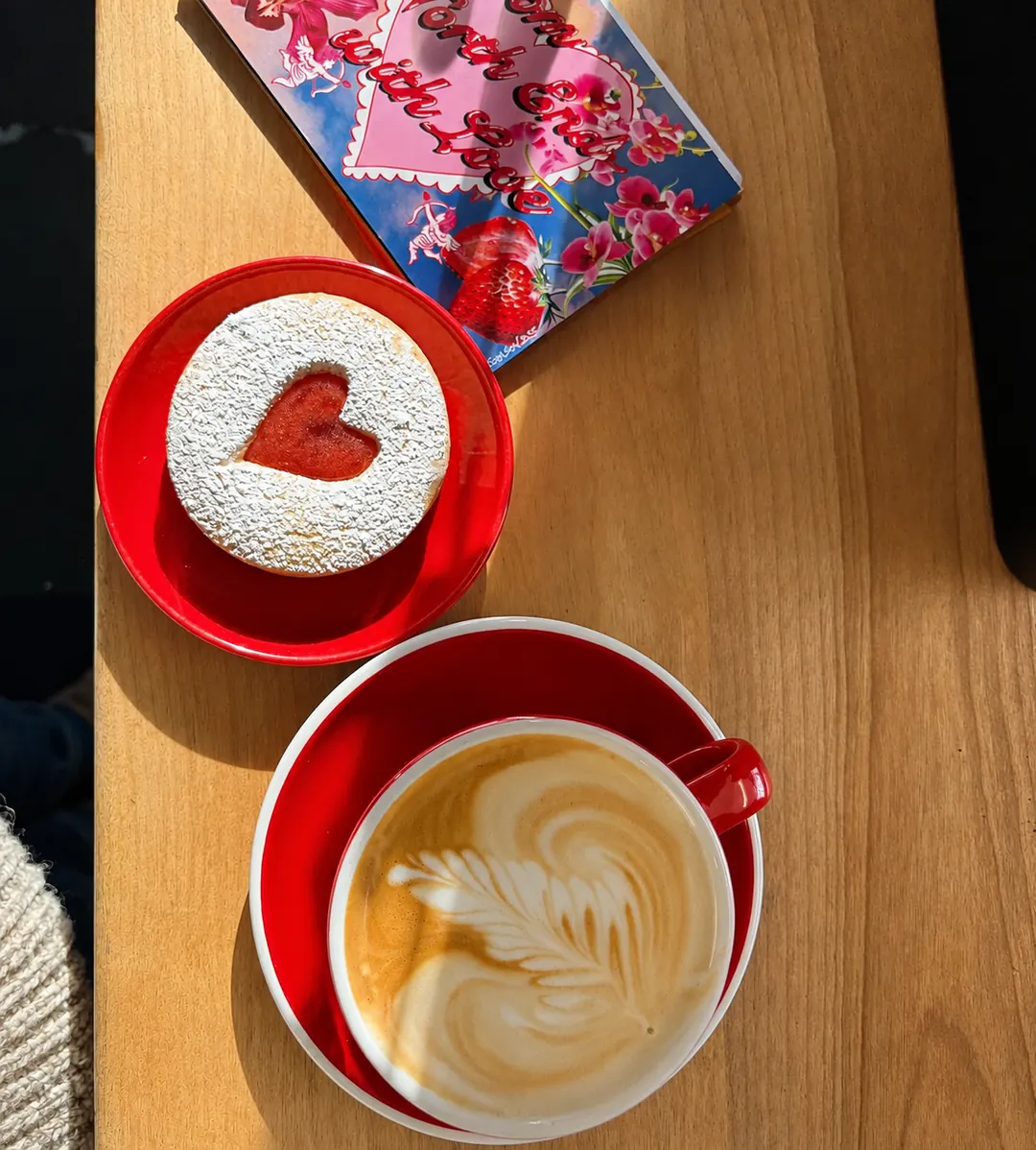 A red coffee cup and a heart-shaped biscuit in the sunlight
