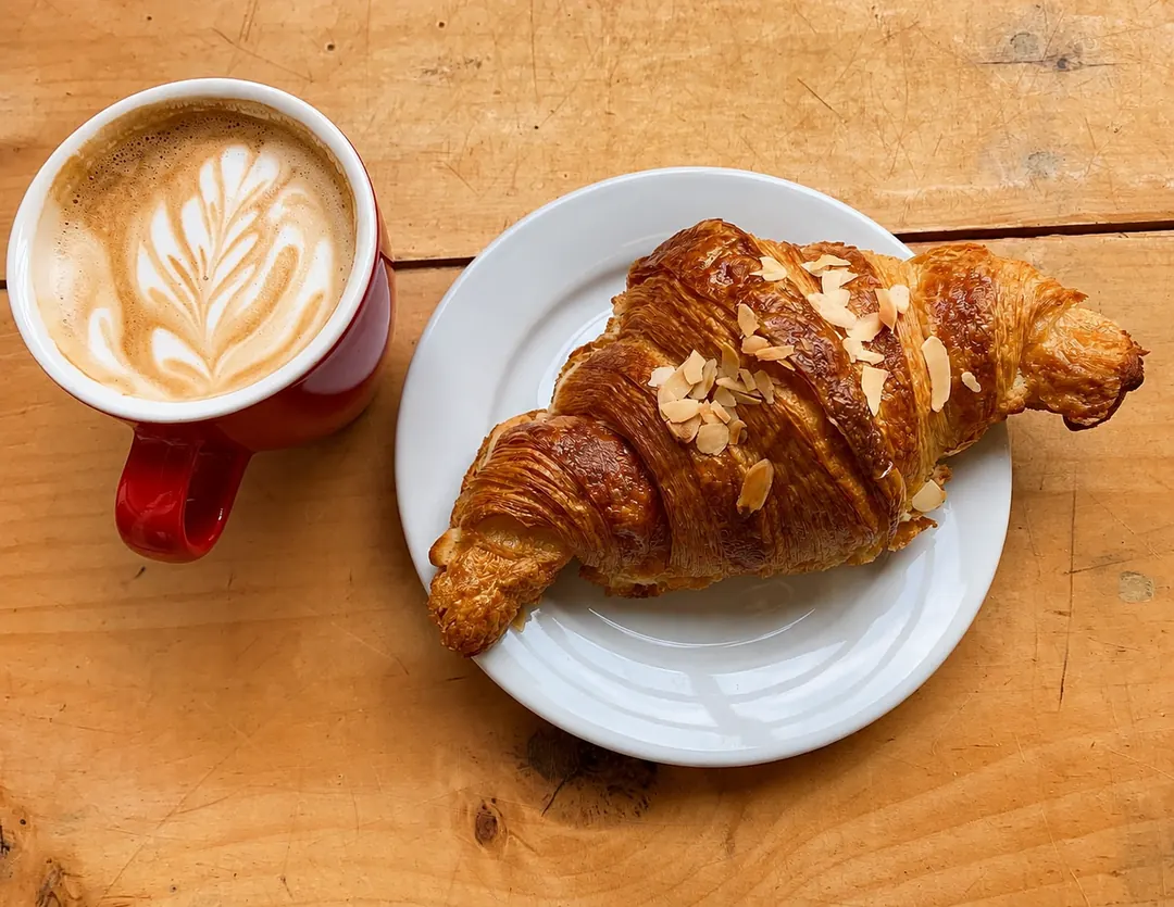 A red cup of coffee beside an almond-topped croissant